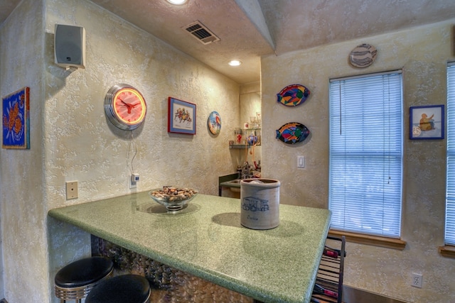 kitchen featuring visible vents, a textured wall, and a kitchen bar