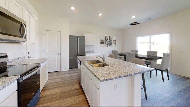 kitchen featuring stainless steel appliances, a sink, light wood-style flooring, and white cabinetry