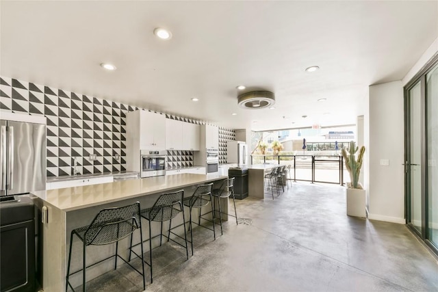 kitchen featuring a spacious island, appliances with stainless steel finishes, a breakfast bar area, finished concrete floors, and light countertops