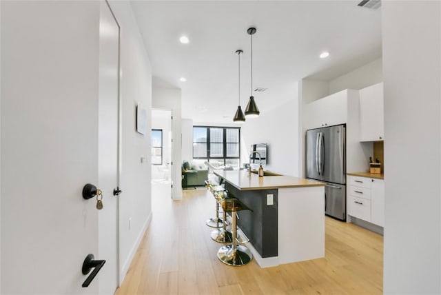 kitchen featuring light wood-style floors, a sink, freestanding refrigerator, and white cabinetry