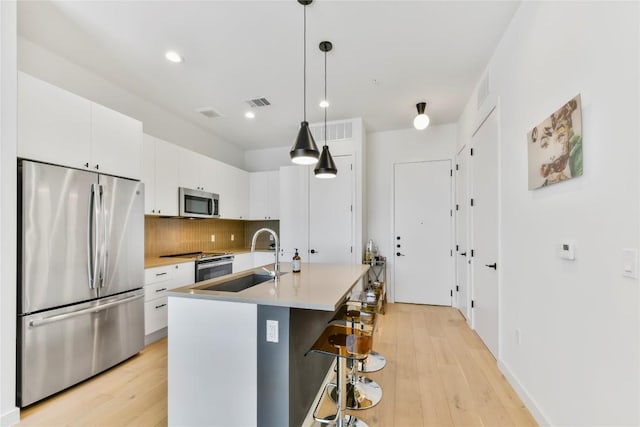 kitchen with stainless steel appliances, tasteful backsplash, light wood-style floors, white cabinets, and a sink