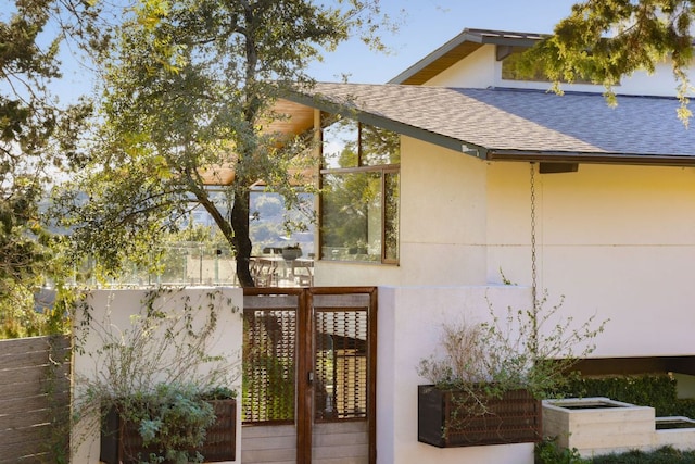 view of exterior entry featuring fence, a shingled roof, and stucco siding