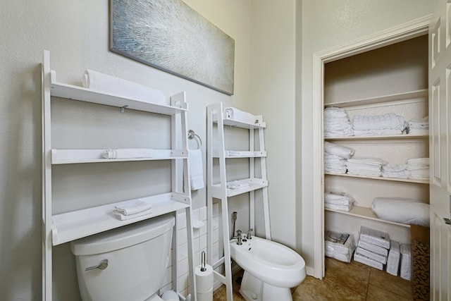 bathroom with toilet, a bidet, and tile patterned floors