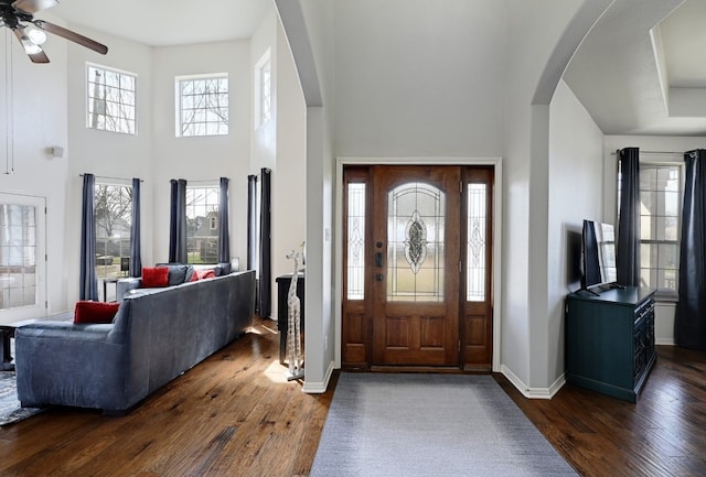 foyer featuring dark wood-style floors, a high ceiling, arched walkways, and baseboards