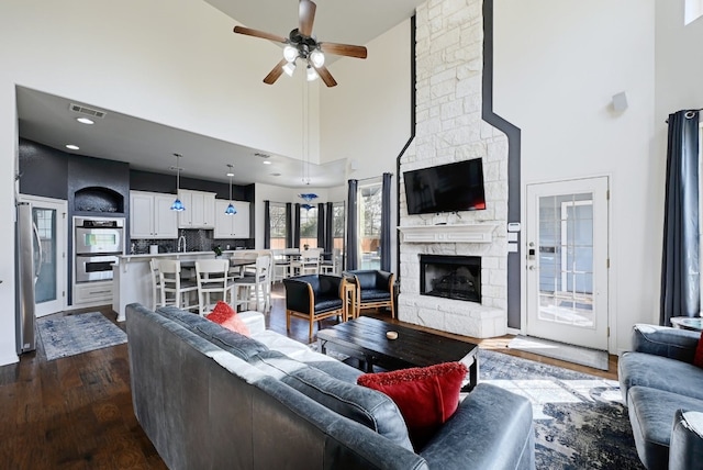 living area featuring a high ceiling, dark wood-style flooring, a fireplace, visible vents, and a ceiling fan