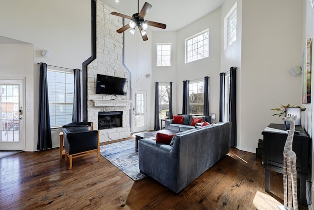 living room with ceiling fan, baseboards, dark wood finished floors, and a stone fireplace