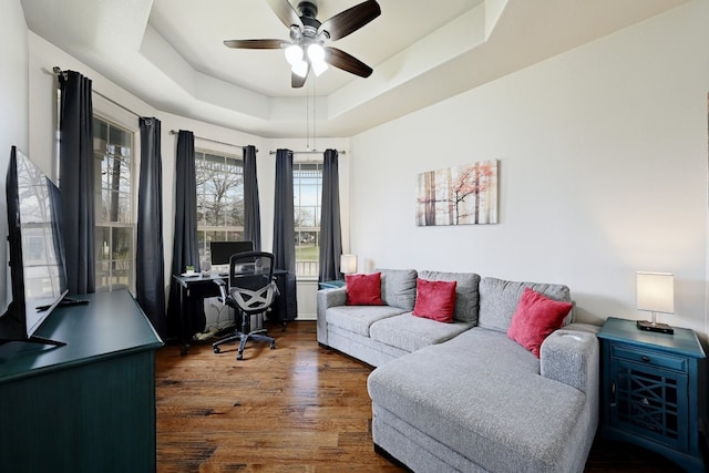 living area with dark wood-style floors, a raised ceiling, and a ceiling fan