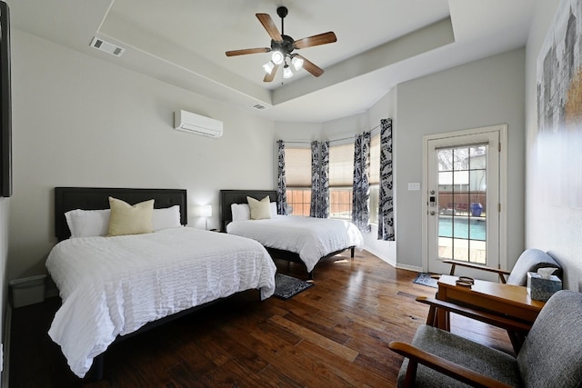 bedroom featuring access to exterior, a raised ceiling, visible vents, a wall mounted AC, and wood finished floors