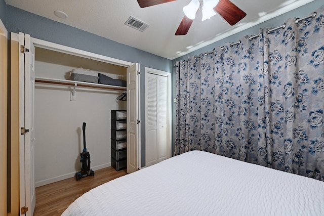 bedroom featuring two closets, visible vents, a ceiling fan, wood finished floors, and baseboards