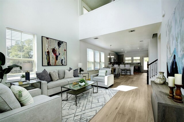 living area with visible vents, light wood-style flooring, a towering ceiling, and stairway