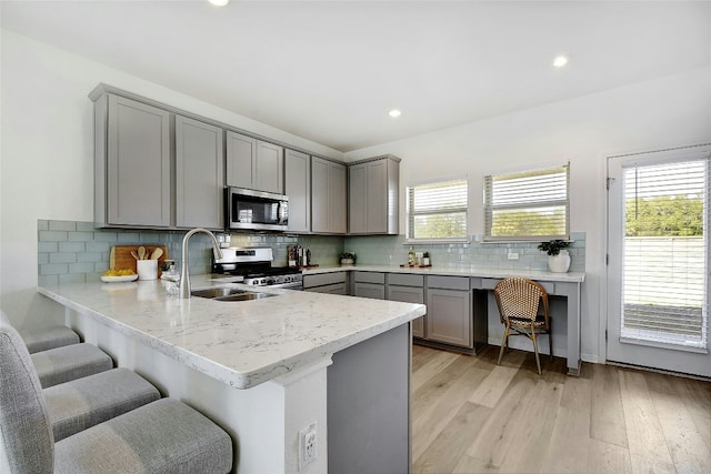 kitchen with a breakfast bar, light wood-style floors, a sink, appliances with stainless steel finishes, and gray cabinetry