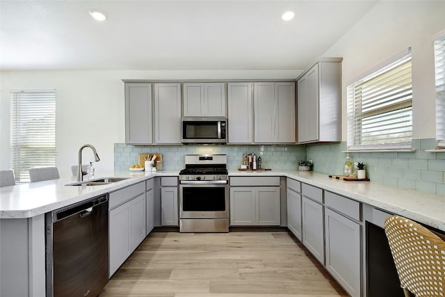 kitchen featuring a peninsula, a sink, appliances with stainless steel finishes, and gray cabinets