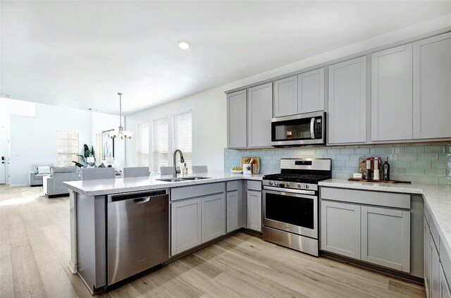 kitchen featuring a sink, light wood finished floors, gray cabinets, stainless steel appliances, and a peninsula