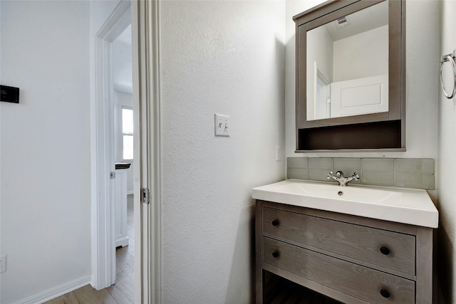 bathroom featuring vanity, wood finished floors, visible vents, and tasteful backsplash