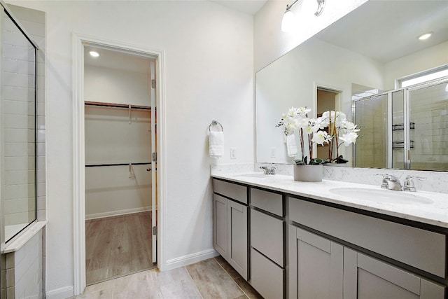 full bath featuring a sink, a walk in closet, a shower stall, and wood finished floors