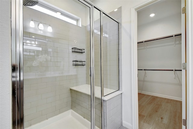 full bath with baseboards, a walk in closet, wood finished floors, and a stall shower
