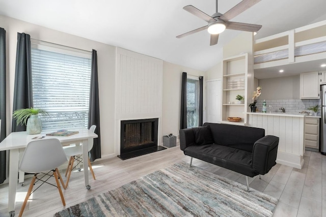 living area featuring lofted ceiling, a large fireplace, ceiling fan, and light wood-style floors