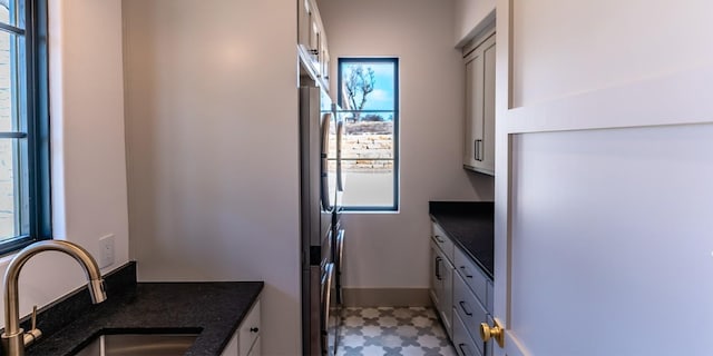 kitchen featuring refrigerator, a sink, baseboards, light floors, and dark stone countertops