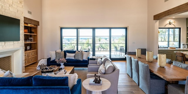 living area featuring a large fireplace, a high ceiling, wood finished floors, and a healthy amount of sunlight