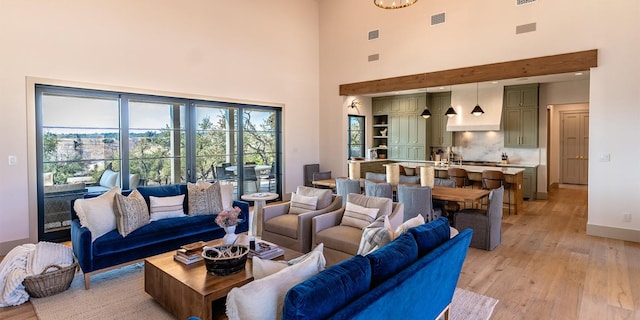 living room with light wood finished floors, visible vents, a high ceiling, and baseboards