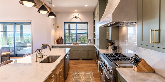 kitchen featuring stainless steel appliances, a sink, visible vents, wall chimney range hood, and light stone countertops