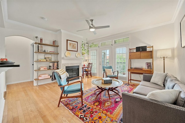 living area with light wood-type flooring, a fireplace, a ceiling fan, and crown molding