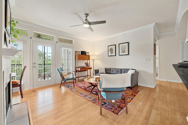 living room featuring a ceiling fan, light wood-style flooring, ornamental molding, and a tiled fireplace