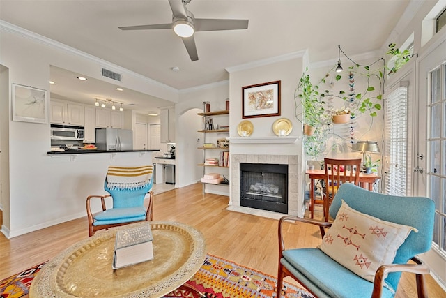 sitting room with light wood-type flooring, visible vents, crown molding, and a tiled fireplace