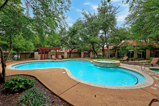 view of pool featuring a pool with connected hot tub, a patio, fence, and a pergola