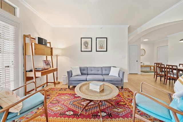 living room featuring ornamental molding, arched walkways, a healthy amount of sunlight, and light wood finished floors