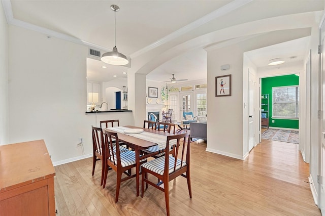 dining room with arched walkways, light wood finished floors, visible vents, and ornamental molding