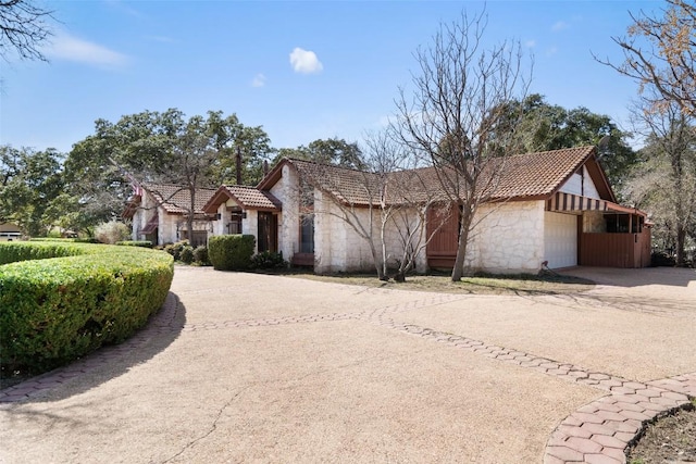 view of front of house with an attached garage, concrete driveway, stone siding, and a tiled roof