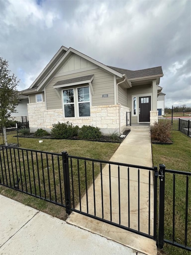 view of front of property with stone siding, board and batten siding, a front yard, and a fenced front yard