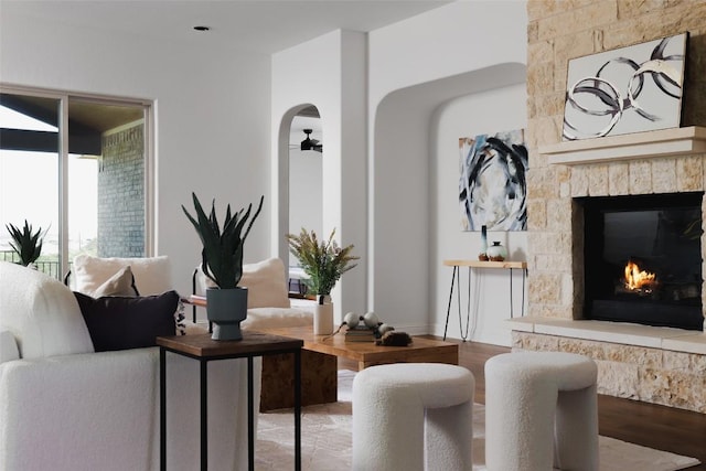 living room with a fireplace, a ceiling fan, arched walkways, and wood finished floors