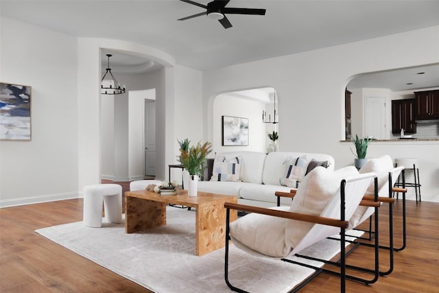 living room with baseboards, arched walkways, wood finished floors, and ceiling fan with notable chandelier