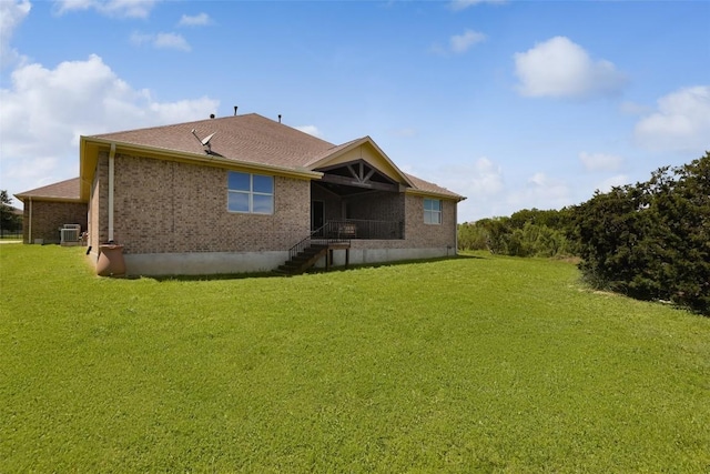 back of house with central AC unit, a lawn, and brick siding