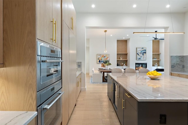 kitchen featuring a spacious island, light stone counters, light wood-style floors, a glass covered fireplace, and modern cabinets