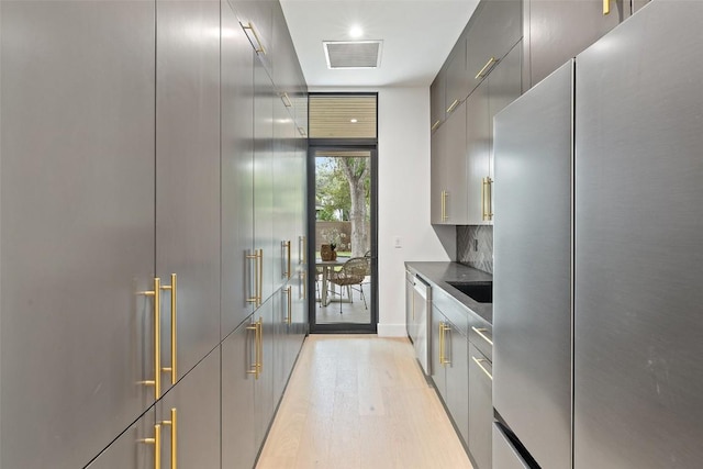 kitchen featuring visible vents, modern cabinets, light wood-style flooring, stainless steel appliances, and decorative backsplash