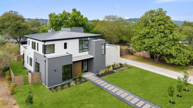 rear view of property with stucco siding, a standing seam roof, fence, a yard, and metal roof