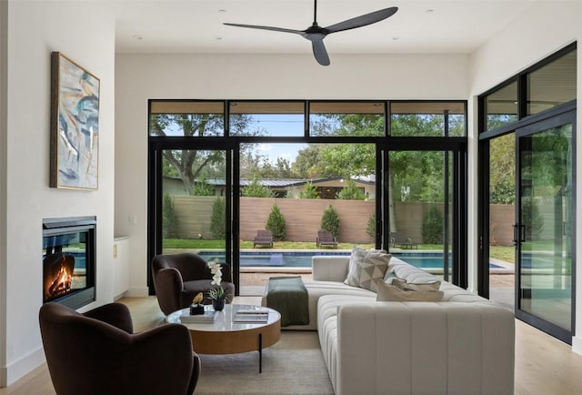 living area featuring a glass covered fireplace, baseboards, and ceiling fan