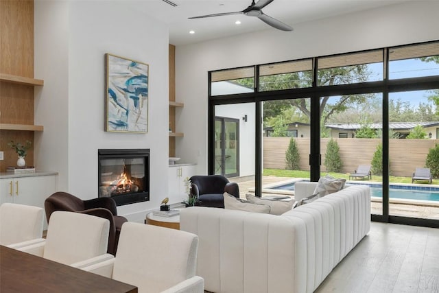 living area with light wood finished floors, a glass covered fireplace, recessed lighting, and built in features