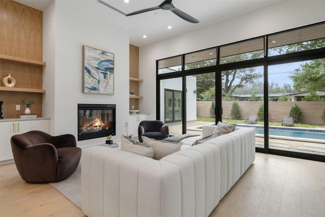 living room with built in shelves, a ceiling fan, recessed lighting, light wood-style floors, and a glass covered fireplace