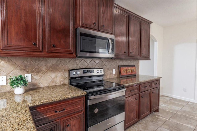 kitchen featuring arched walkways, stainless steel appliances, baseboards, decorative backsplash, and light stone countertops