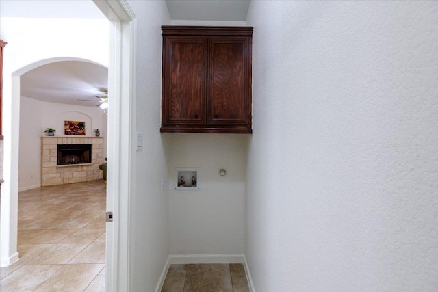 washroom with cabinet space, baseboards, a ceiling fan, hookup for a washing machine, and a stone fireplace