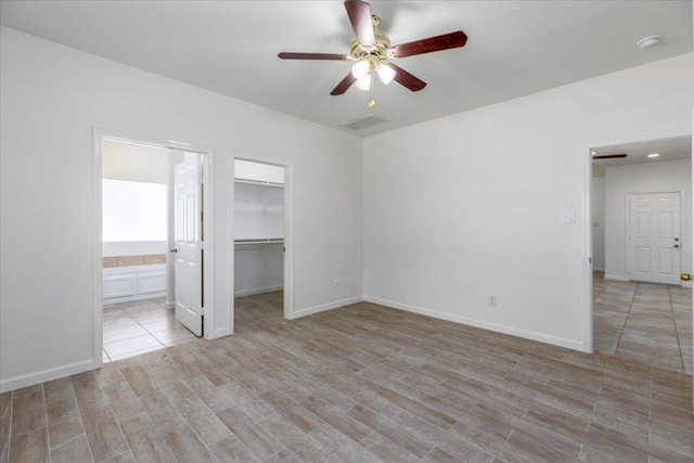 unfurnished bedroom featuring a closet, a spacious closet, ensuite bath, light wood-type flooring, and baseboards