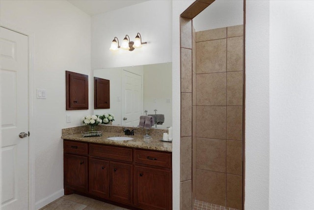 bathroom featuring tile patterned flooring, tiled shower, vanity, and baseboards