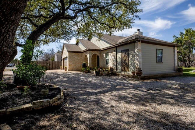 view of front of home featuring stone siding, a chimney, gravel driveway, and fence