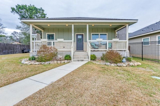 view of front of house with board and batten siding, a front yard, covered porch, and fence