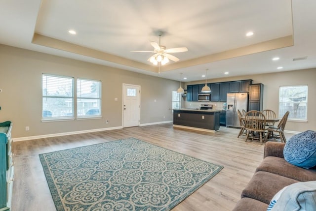 living area featuring light wood finished floors, recessed lighting, a raised ceiling, ceiling fan, and baseboards