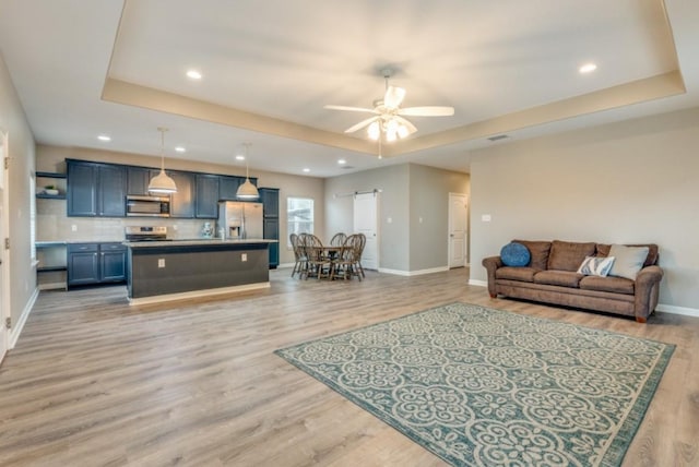 living area featuring light wood-style floors, a barn door, a raised ceiling, and ceiling fan